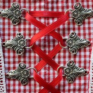 Puede incluir: Primer plano de una tela de cuadros rojos y blancos con cierres de metal plateado y una cinta roja atada en forma de cruz.