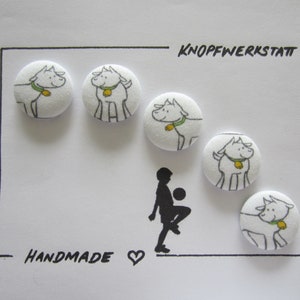 Könnte beinhalten: Fünf weiße Stoffknöpfe mit einer schwarz-weißen Illustration eines Hundes, der ein grünes Halsband mit einer gelben Glocke trägt. Die Knöpfe sind in einem Halbkreis angeordnet, mit dem Text "KNOPFWERKSTATT" und "HANDMADE" oben und unten im Bild.