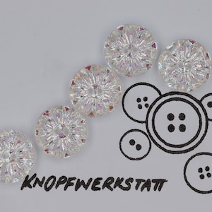 May include: Five iridescent clear glass buttons with a starburst design. The buttons are arranged in a diagonal line. The word "KNOPFWERKSTATT" is written in black ink below the buttons.
