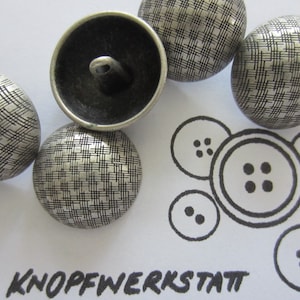 May include: Five silver metal buttons with a textured, crosshatch pattern. The buttons are round and have a raised center. The buttons are arranged in a semi-circle on a white surface. The text "KNOFFWERKSTATT" is written in black ink at the bottom of the image.