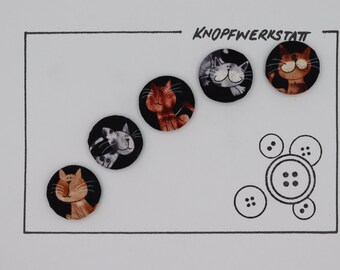 Puede incluir: Cinco botones redondos de tela con diseños de gatos. Los botones son negros con caras de gatos blancas y naranjas. El texto "KNOFFWERKSTATT" está escrito en negro en la parte superior de la imagen.