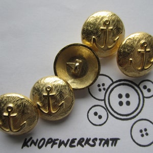 Könnte beinhalten: Fünf goldfarbene Metallknöpfe mit Anker-Design. Die Knöpfe haben eine strukturierte Oberfläche.