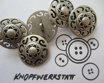 May include: A set of six silver metal buttons with intricate designs. The buttons feature a floral pattern with a raised center and a black outline. The buttons are arranged in a semi-circle on a white surface.
