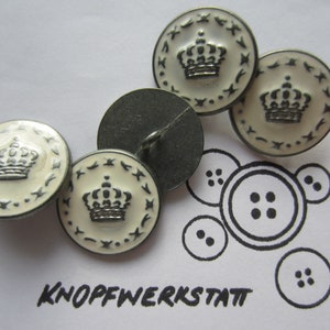 Könnte beinhalten: Vier weiße Knöpfe mit einem silbernen Kronendesign und schwarzem Besatz. Die Knöpfe befinden sich auf einer weißen Oberfläche mit dem in Schwarz geschriebenen Text "KNOFFWERKSTATT".