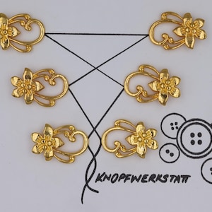 Puede incluir: Seis adornos de metal dorado con un diseño floral. Cada adorno presenta una flor estilizada con un bucle en el lateral.