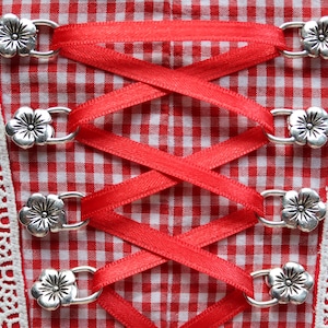 Puede incluir: Tela de cuadros rojos y blancos con cordones de cinta roja y cierres de metal plateado en forma de flor.
