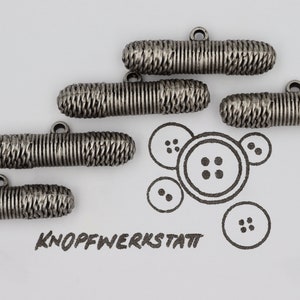 Könnte beinhalten: Fünf silberne Metall-Toggle-Knöpfe mit einem strukturierten, gewebten Design. Die Knöpfe haben eine Schlaufe oben zum Anbringen an Stoff.