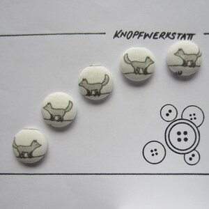 May include: Five white fabric buttons with a gray fox design. The buttons are arranged in a semi-circle on a white background. The text "KNOFFWERKSTATT" is written in black at the top of the image.