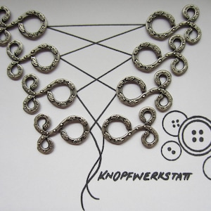 May include: Silver metal decorative loops with a textured surface. The loops are arranged in a pattern on a white background. The text "Knopfwerkstatt" is written in black below the loops.
