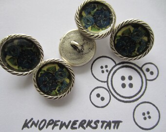 May include: Five decorative buttons with a floral design in shades of blue and green, set against a pale yellow background, encased in a silver-colored, rope-textured frame. The word "KNOPFWERKSTATT" is written in black ink.