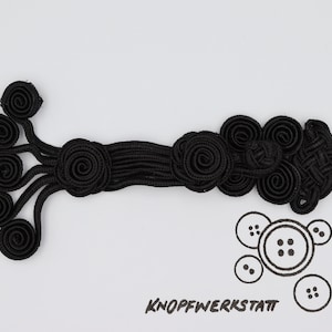 May include: Black Chinese knot closure with a decorative design. The knot is made of braided fabric and has a series of loops and knots.