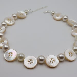 Puede incluir: Un collar de perlas blancas y botones de nácar. El collar está hecho con perlas blancas y botones de nácar alternados.