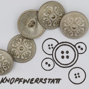 May include: Five silver buttons with an ornate design. The buttons have a raised center and a decorative border. The buttons are arranged in a semi-circle on a white background. The word "KNOPFWERKSTATT" is written in black ink below the buttons.