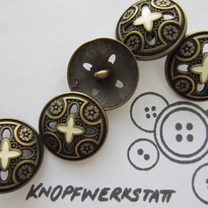 Könnte beinhalten: Vier verzierte Metallknöpfe mit einem weißen Kreuzdesign und einer goldenen Oberfläche. Die Knöpfe haben einen dekorativen Rand mit einem Blumenmuster. Die Knöpfe sind in einer Reihe auf einer weißen Oberfläche angeordnet.