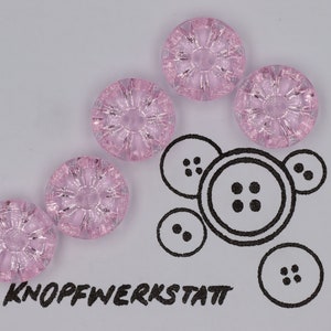 May include: Five pink glass buttons with a decorative design. The buttons are arranged in a semi-circle on a white surface. The word "KNOFFWERKSTATT" is written in black ink below the buttons.
