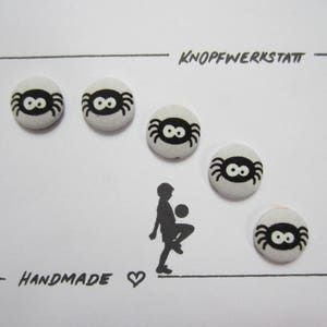 Könnte beinhalten: Fünf schwarze und weiße Spinnenknöpfe mit dem Text "KNOPFWERKSTATT" und "HANDMADE" auf weißem Hintergrund.