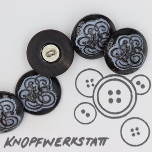 Könnte beinhalten: Fünf schwarze Knöpfe mit einem weißen Wirbelmuster. Die Knöpfe sind in einem Halbkreis angeordnet. Das Wort "KNOPFEWERKSTATT" ist in Schwarz am unteren Rand des Bildes geschrieben.