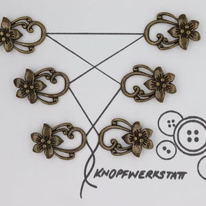 May include: Six antique gold-toned metal flower embellishments with a decorative swirl design.