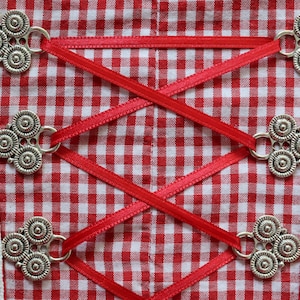Puede incluir: Tela a cuadros rojos y blancos con cuatro cierres de metal plateado y cordones de cinta roja.