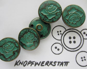 Op de afbeelding: Een verzameling ronde, teal-kleurige knopen met een rozenontwerp en een bijpassende schachtknop. De knopen hebben een verweerde, antieke afwerking met een bronskleurige rand. Het woord "KNOPFWERKSTATT" staat onderaan.