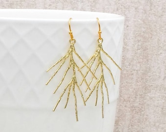 May include: A pair of gold-toned dangle earrings featuring a textured, branch-like design that mimics the appearance of small twigs. Each earring hangs from a simple gold-toned hook, showcasing a detailed, organic structure with multiple thin, pointed extensions radiating outward.