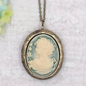 May include: A gold-tone locket necklace with a cameo of a woman's profile. The cameo is white with a blue background and features a floral design.