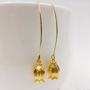 May include: A pair of gold-tone earrings with a bell-shaped design. The earrings are made of metal and have a long, thin drop.