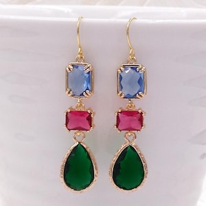 May include: Gold-toned drop earrings with three colorful gemstone accents. Each earring features a blue rectangular top stone, a red square center stone, and a green teardrop-shaped bottom stone. The earrings are displayed against a white background.
