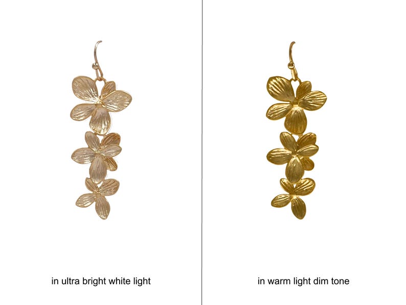 May include: Gold-colored floral earrings. Each earring features three flower-shaped pendants hanging from a hook. The image shows the earrings in two different lighting conditions: ultra bright white light and warm light dim tone.