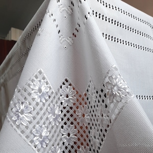 May include: White tablecloth with a delicate floral embroidery pattern. The embroidery features a grid of small white flowers.