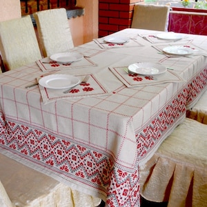 Pu&ograve; includere: Una tovaglia di lino bianco con motivi geometrici ricamati in rosso e nero. La tovaglia &egrave; stesa su un tavolo di legno con piatti bianchi e posate.