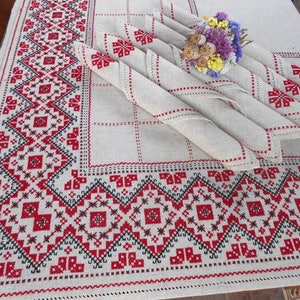 Pu&ograve; includere: Una tovaglia di lino bianco con un bordo ricamato rosso e nero. La tovaglia &egrave; decorata con diversi tovaglioli di lino piegati con motivi ricamati rossi e neri.