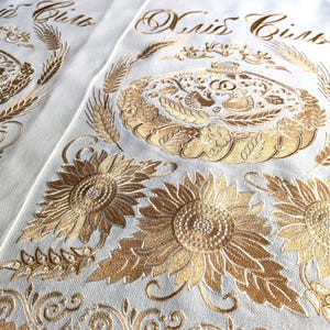 Könnte beinhalten: Zwei weiße Stoffbahnen mit goldener Stickerei. Die Bahnen zeigen ein florales Design mit Sonnenblumen und Weizenähren. Der Text "Maid Gifts" ist auf jede Bahn gestickt.