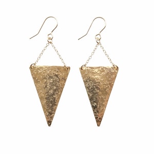 May include: A pair of gold-colored earrings with a textured, triangular pendant. The earrings hang from a chain and hook. The pendants are approximately 2 inches long.