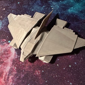 Puede incluir: Un modelo de nave espacial impreso en 3D de color gris con un diseño futurista. El modelo está detallado con ángulos agudos y una nariz puntiaguda.