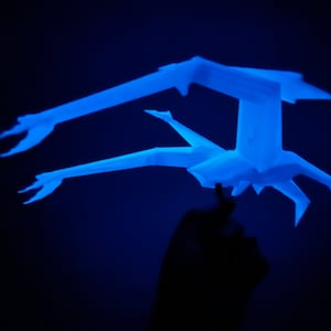 May include: A blue paper sculpture of a bird in flight. The sculpture is lit from below, casting a shadow on the background.