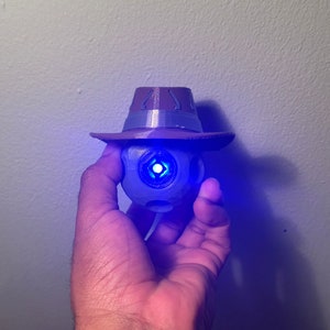 Op de afbeelding: Een 3D-geprint beeldje van een robot in blauw en grijs, met een bruine cowboyhoed. De robot heeft een blauw licht in zijn oog.