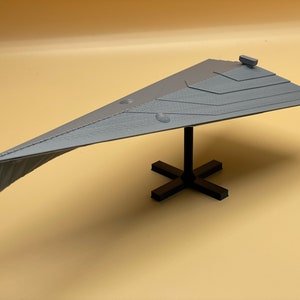 Puede incluir: Un modelo gris de un destructor estelar Star Destroyer impreso en 3D sobre una base negra.