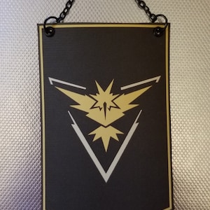 May include: A black banner with a gold and white stylized bird logo. The banner has a chain attached to the top for hanging.