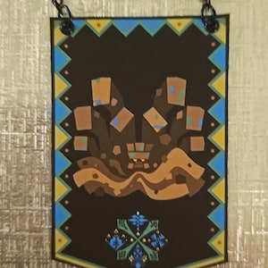 Puede incluir: Un banner marrón y negro con una cadena para colgar. El banner presenta una imagen estilizada de un monstruo con un esquema de color marrón, naranja y azul. El banner tiene un borde de patrón geométrico en amarillo, azul y verde.