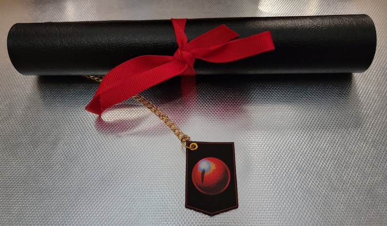 May include: A black rolled-up tube tied with a red ribbon and a gold chain with a black tag featuring a red orb with a white streak.