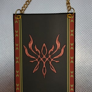 May include: A black banner with a gold chain for hanging. The banner features a stylized red crest with flames and a diamond shape in the center. The banner has a red and gold border with a repeating pattern.