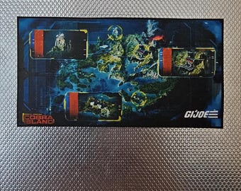 Puede incluir: Un tablero de juego GI Joe rectangular con un mapa con varias ubicaciones. El tablero tiene un fondo azul oscuro con masas terrestres amarillas y verdes. Las palabras "COBRA ISLAND" y "GI JOE" son visibles.