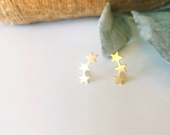 May include: A pair of gold star shaped earrings. Each earring has three stars in a curved line.