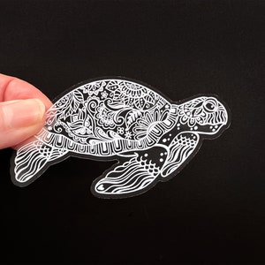 May include: A white vinyl sticker of a detailed, ornate sea turtle with a black background.
