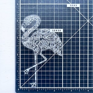 May include: A clear sticker featuring a white flamingo design. The flamingo is intricately detailed with floral and geometric patterns. The sticker measures approximately 2.5 x 3.5 inches. The flamingo is standing on one leg, with its head and neck curved.