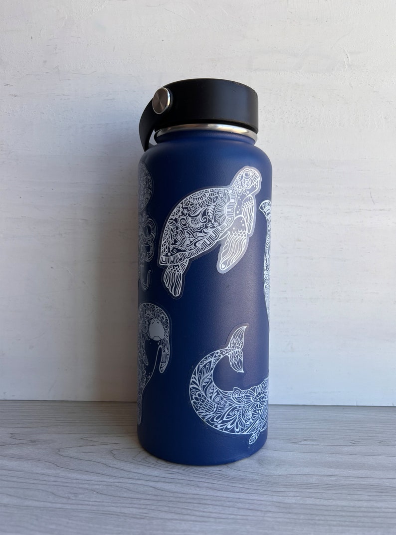 May include: A blue reusable water bottle with white, intricate designs of sea creatures, including a turtle, a whale, and a manatee.