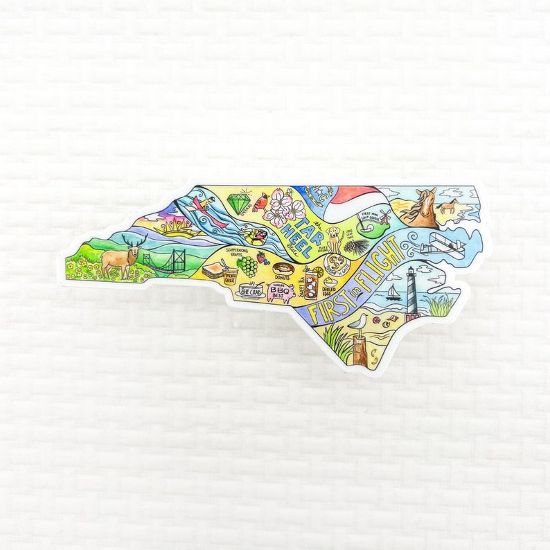 May include: A colorful sticker in the shape of North Carolina, featuring illustrations of state symbols and landmarks. The sticker includes the text "Tar Heel" and "First in Flight", along with images of a deer, lighthouse, and horse.