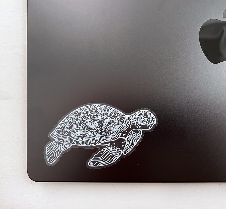 May include: A white sticker of a detailed, ornate sea turtle with a floral pattern on a black laptop.