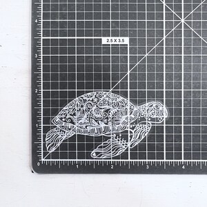 May include: A white, detailed, intricate, and ornate sticker of a sea turtle. The turtle is facing right and has a detailed shell and body.